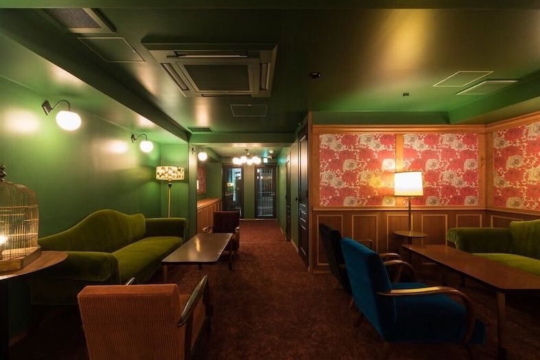 BAR TAMBI｜グリーンの壁と赤い絨毯の床が続き、奥にはソファ席が見える構図で、バーの奥行きある空間が伝わるカット