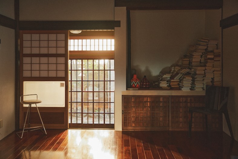 出汁　北千住古民家｜【1階】西陽が差し込む裏側入口と積み上げられた書籍