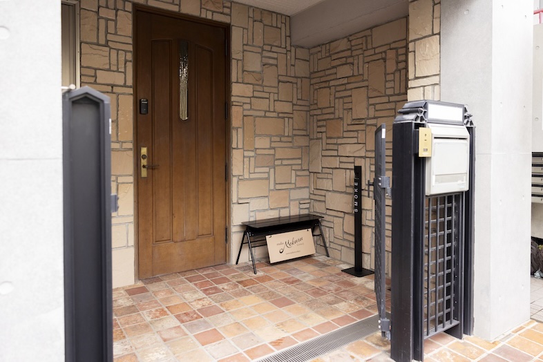 Studio Mekuru｜【1F Prologue】タイル床と石壁が印象的なアプローチとStudio Mekuru ロゴサインがゲストを迎える