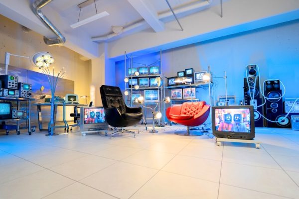 白いグリッド空間にブラウン管テレビやヴィンテージ機材が並ぶ近未来的なセット