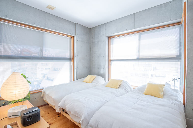 apartment2122｜二面の大きな窓を背景にベッドが並ぶ明るい寝室